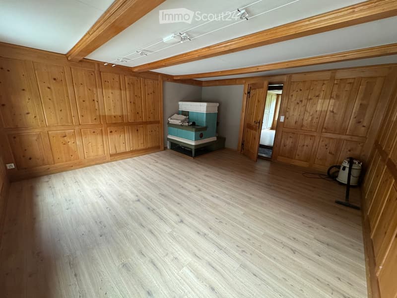 Empty room with wooden walls and floor, a small green and white chest, and a vacuum cleaner in the corner.