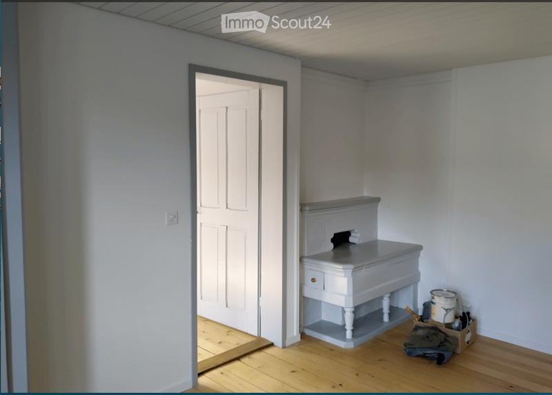 Empty room with wooden flooring, white walls, a small built-in bench, and a partially open door leading to another space.