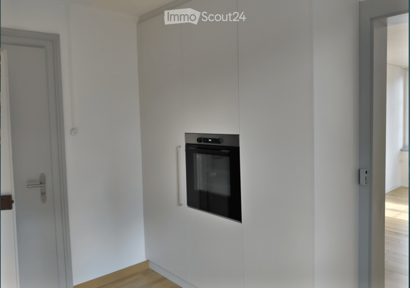 Modern kitchen with white cabinets, a built-in oven, and wooden flooring.