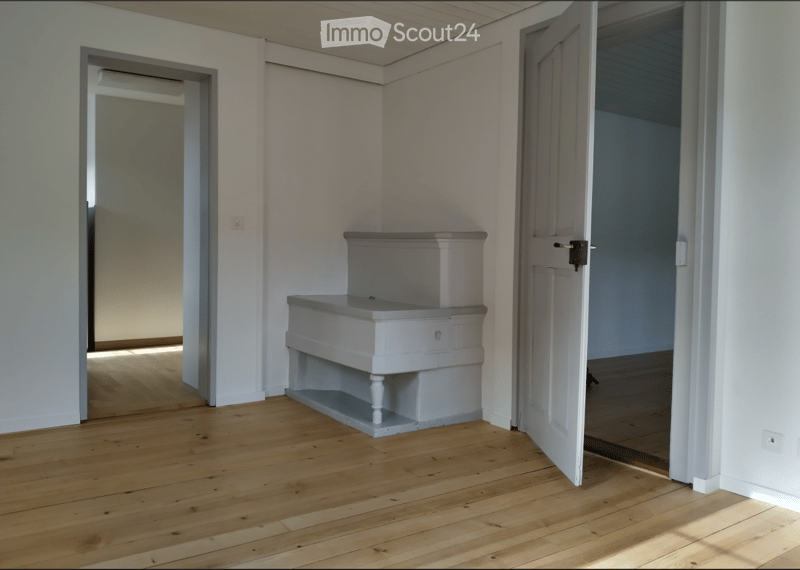 Empty room with wooden flooring, white walls, and a small built-in bench. Two open doors lead to adjacent spaces.