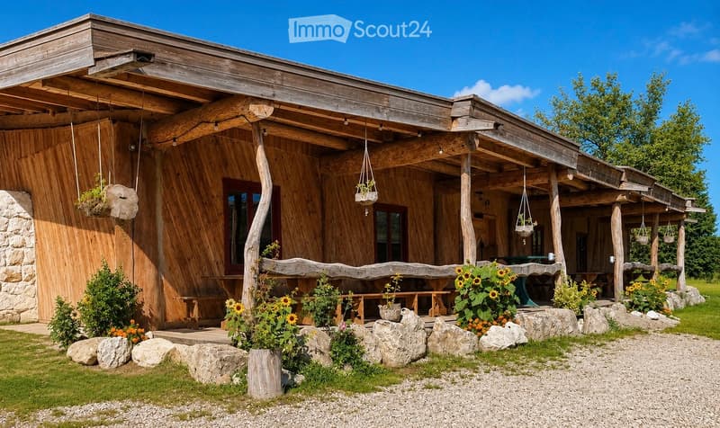 A wooden cabin with a covered porch, surrounded by sunflowers, potted plants, and stone accents. The structure features wooden walls, a slanted roof, and hanging planters.