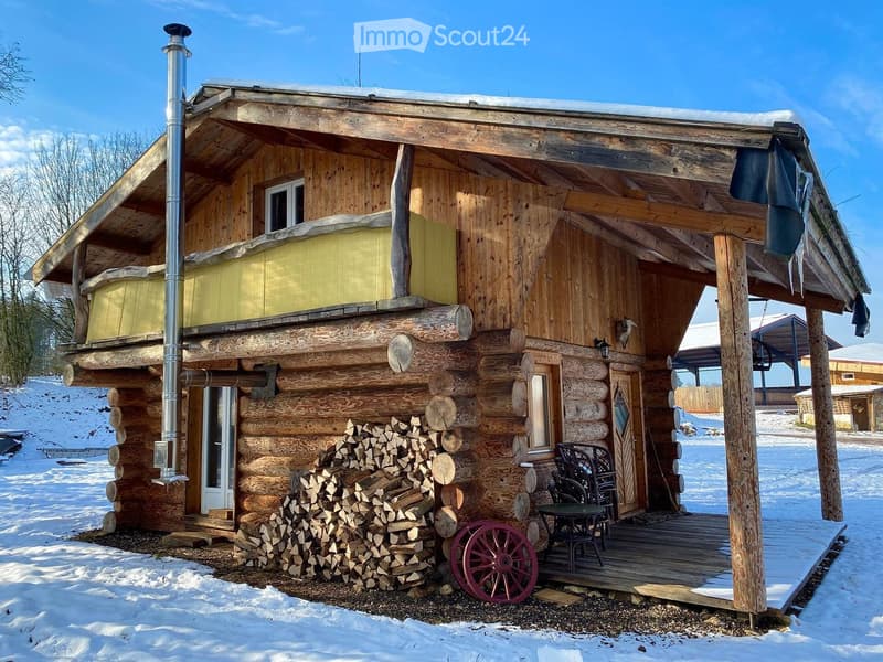 A rustic wooden log cabin with a raised ground floor, chimney, and a porch with outdoor furniture.