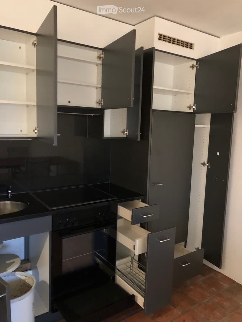 Modern kitchen with black and white cabinets, an oven, and a sink. Open cabinets reveal storage space, and a pot is on the counter.