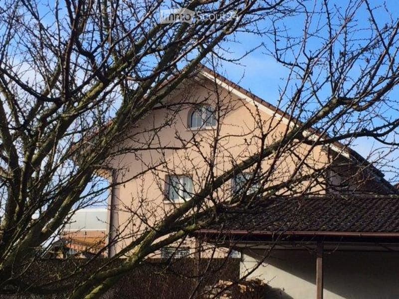 A two-story house with beige walls and multiple windows, partially obscured by leafless trees.