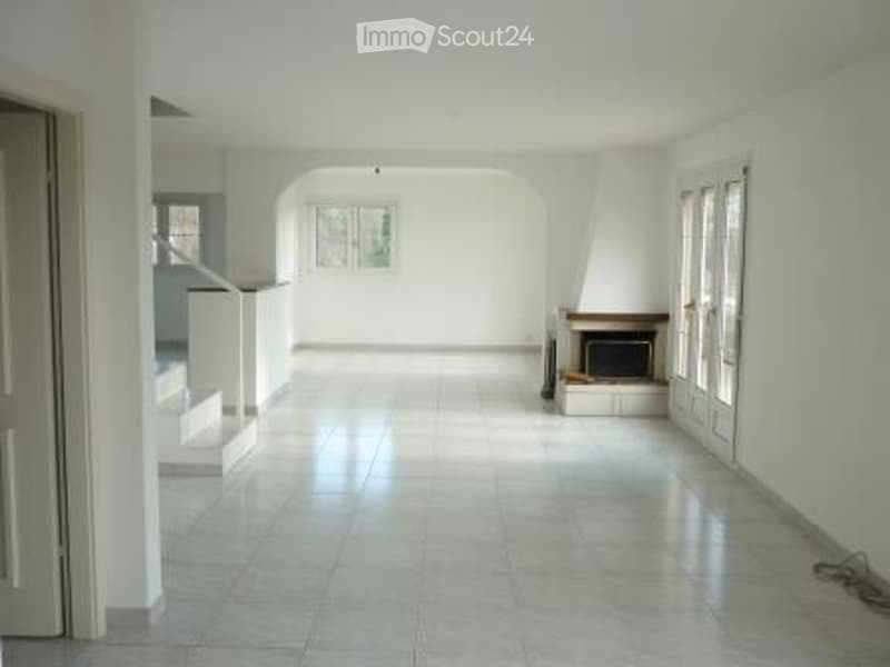 Empty room with white walls, tiled floor, fireplace, and large windows. No furniture or equipment present.