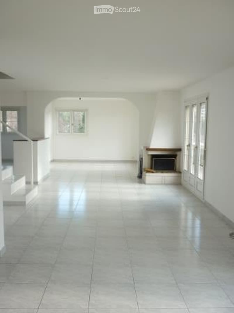 Empty room with white walls, tiled floor, fireplace, and large windows.