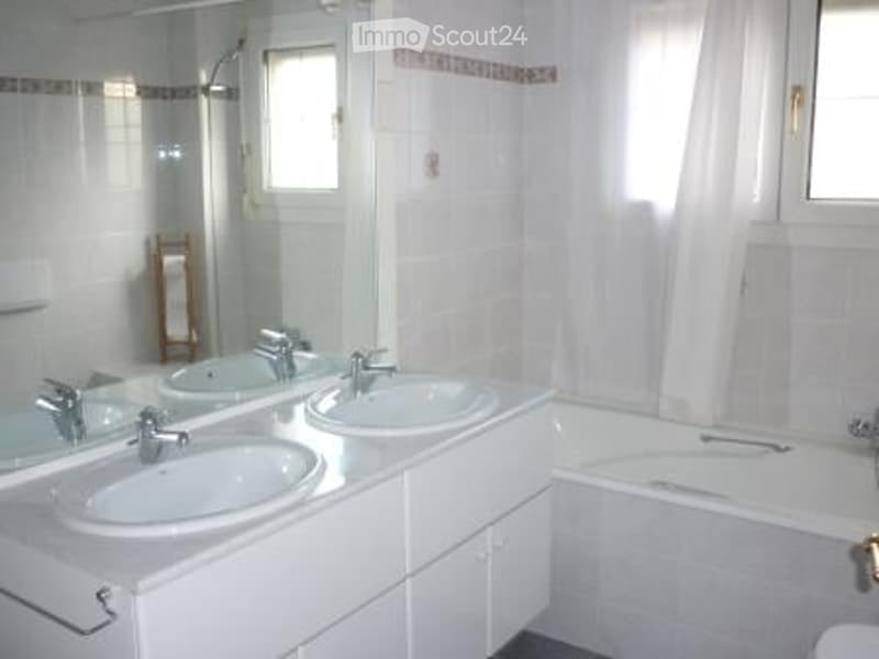 Modern bathroom with white tiles, double sink vanity, large mirror, bathtub, and window with curtain.