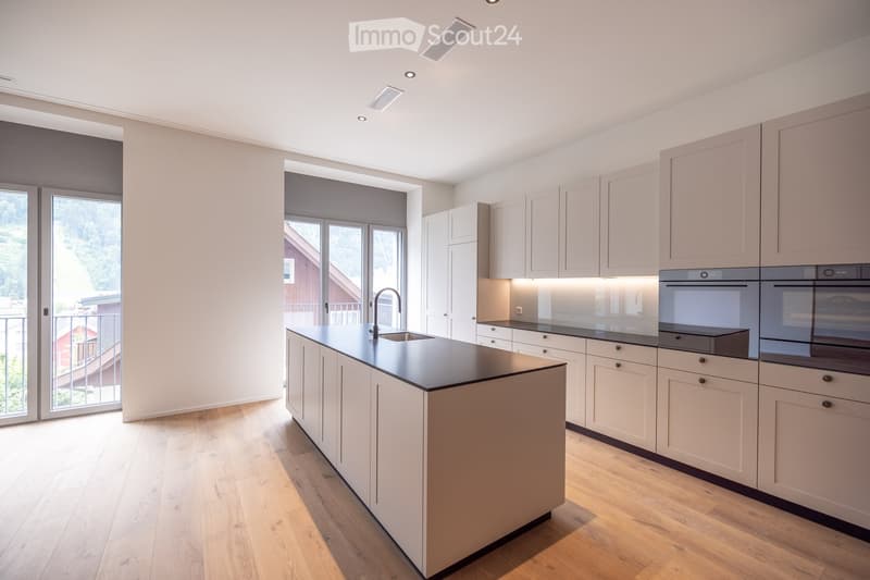 Modern kitchen with light-colored cabinets, a central island, and built-in appliances including an oven and sink.