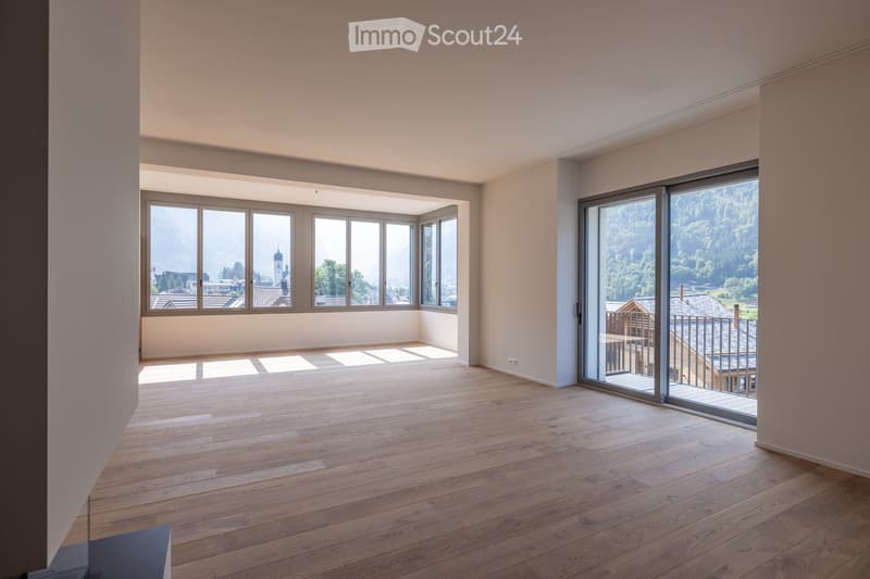 Empty room with wooden flooring, large windows, and a sliding glass door leading to a balcony with a scenic mountain view.