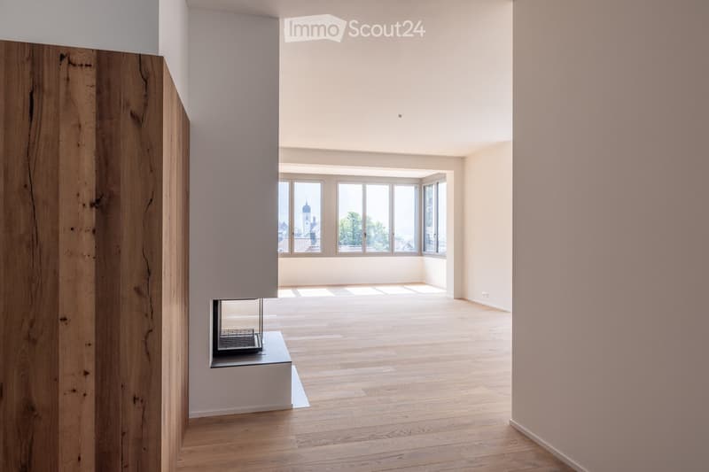 Empty room with wooden flooring, white walls, large windows, and a built-in fireplace.