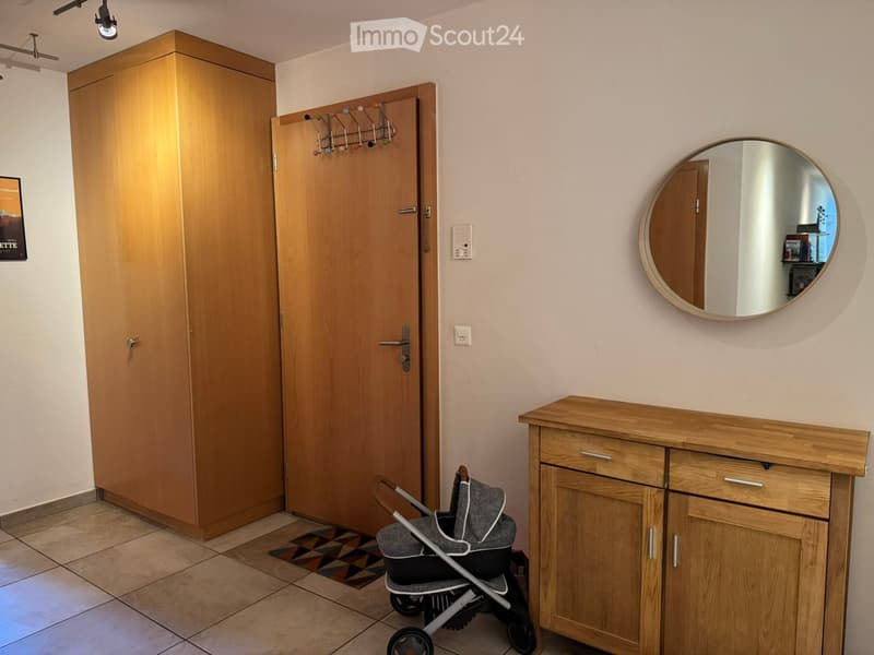 A small hallway with a wooden cabinet, a round mirror, a baby stroller, and a coat rack with hooks.