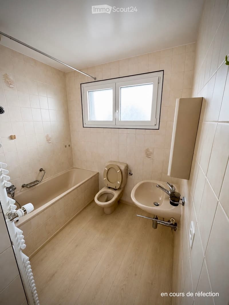 Bathroom with beige tiles, a bathtub, toilet, sink, and a window with white frame.