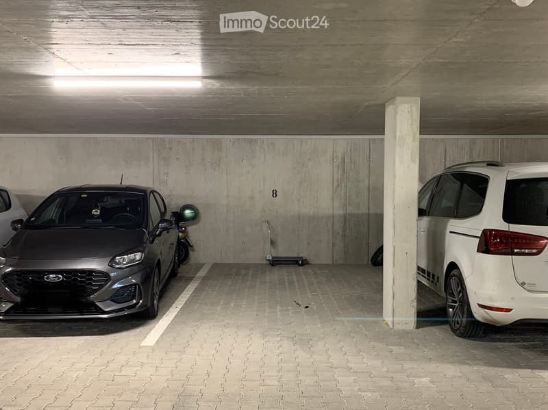 Underground parking area with two cars and a scooter parked, concrete walls and ceiling, tiled floor.