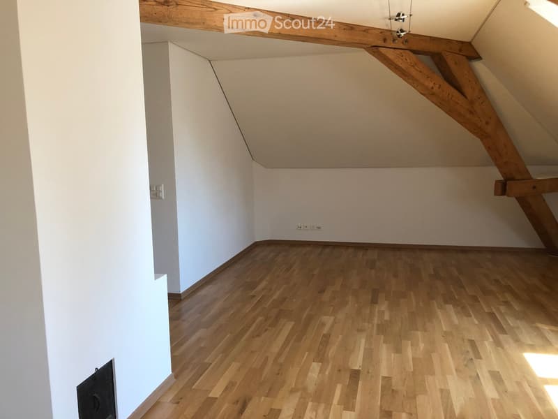 Empty attic room with wooden floor, white walls, and exposed wooden beams on the ceiling.