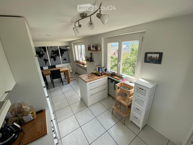 Bright kitchen with white cabinets, wooden countertops, and a dining area. Features include a table with chairs, a small wooden stool, and a world map on the wall.