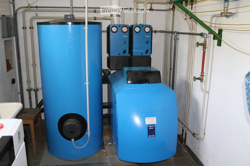 A utility room with a large blue water heater, a Buderus Logano Plus GB125 unit, and various pipes and gauges.