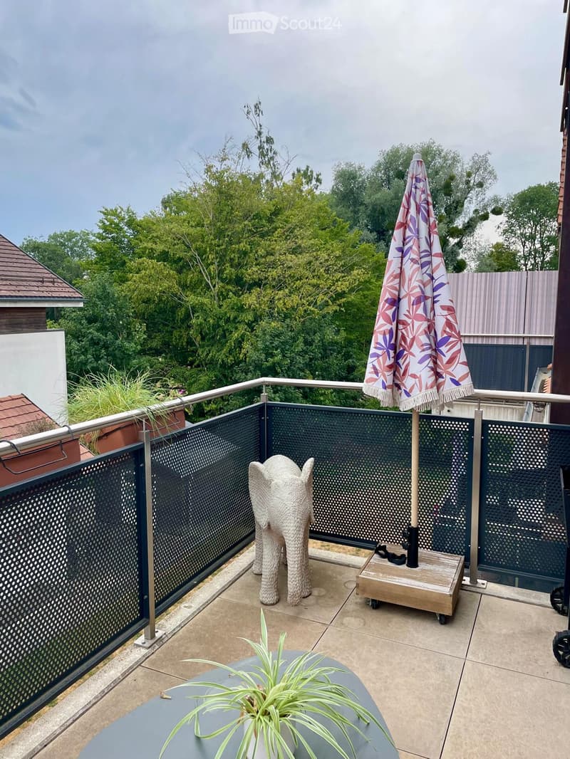 Balcony with a grey table, a decorative elephant chair, a potted plant, and an umbrella on a wooden stand.