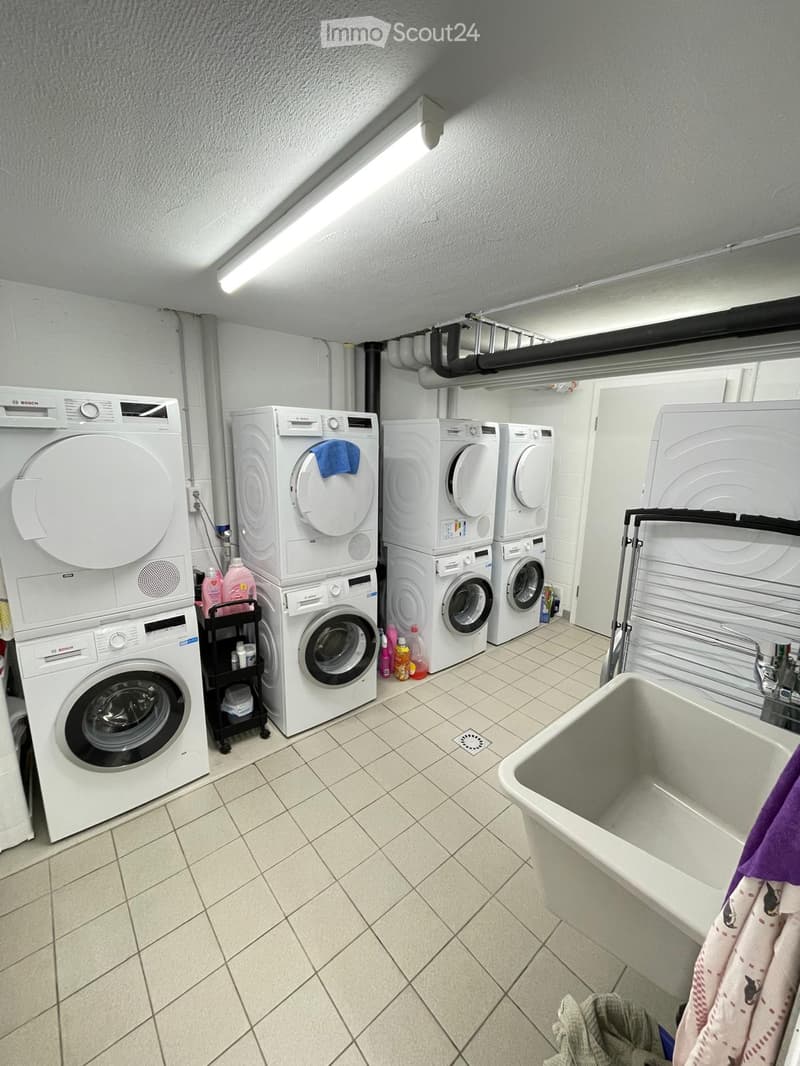 A well-lit laundry room with multiple Bosch washing machines and a dishwasher, a sink, and cleaning supplies on a small cart.
