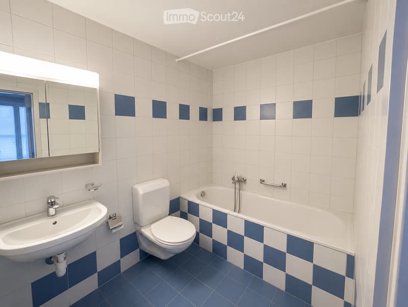 Modern bathroom with white and blue tiles, a sink, toilet, bathtub, and a large mirror above the sink.