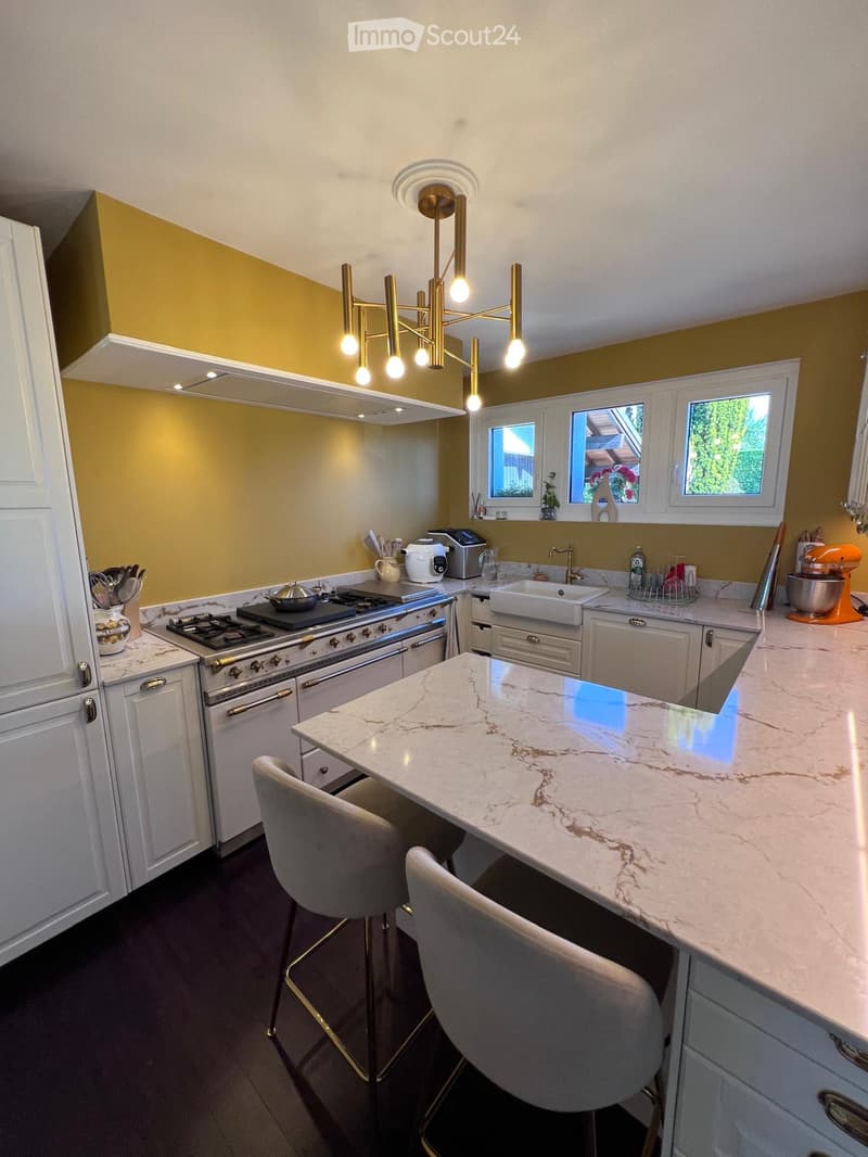 Modern kitchen with white cabinets, marble countertop, gas stove, sink, and bar seating for two.