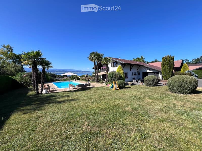 A well-maintained garden with a swimming pool, lounge chairs, and a large house with a garage and balcony.