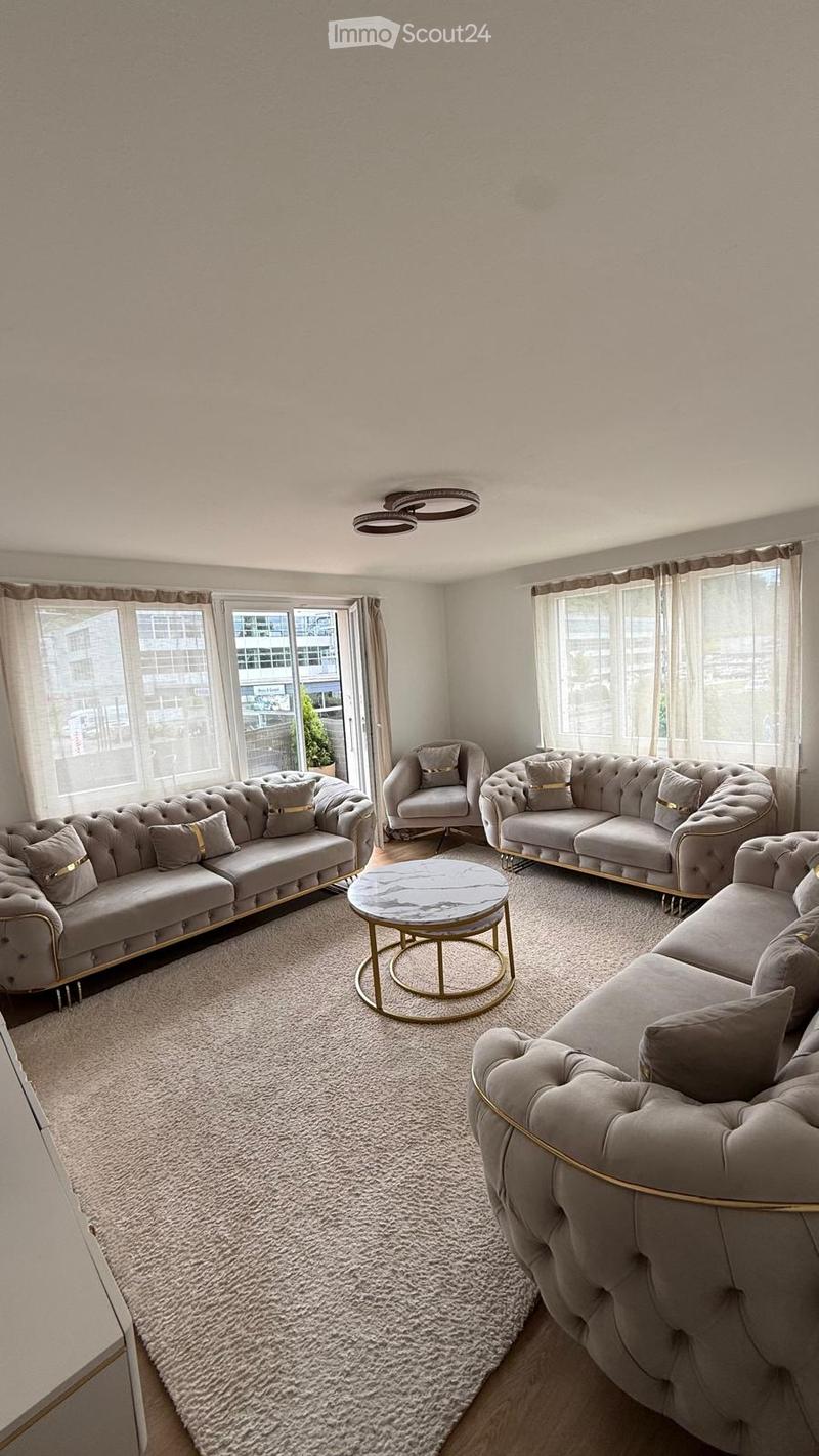 Modern living room with large windows, beige sofas, a round marble coffee table, and a plush white rug.