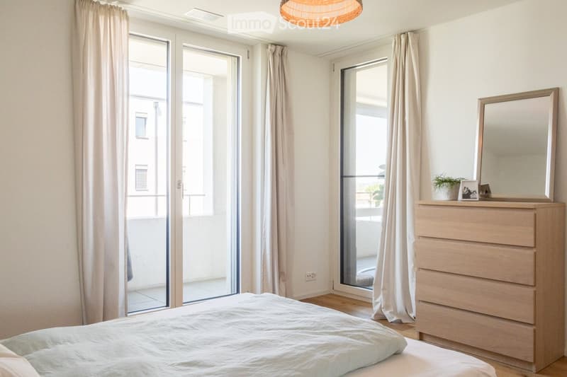 Bright bedroom with a large bed, dresser with mirror, and sliding glass doors leading to a balcony.