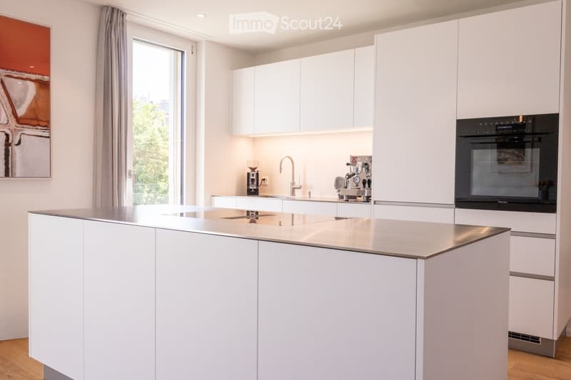 Modern kitchen with white cabinets, a central island, stainless steel sink, coffee maker, and built-in oven.