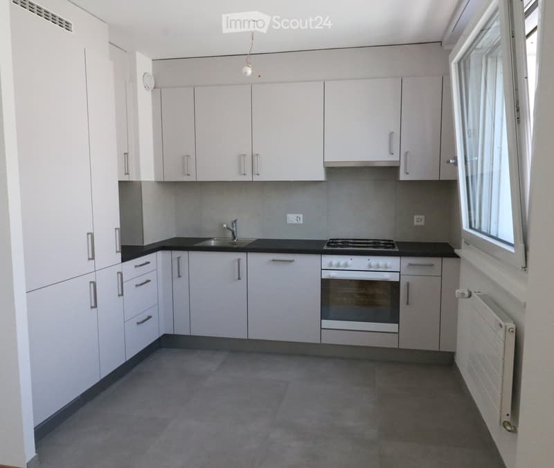 Modern kitchen with white cabinets, black countertops, a sink, a stove, and an oven. The space is well-lit with large windows and has a clean, minimalist design.