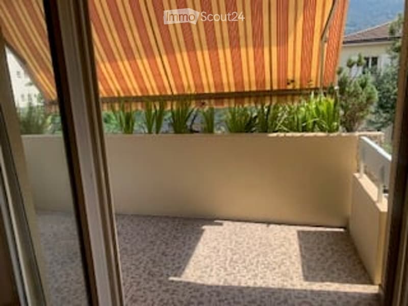 Balcony with striped awning, white railing, tiled floor, and potted plants.