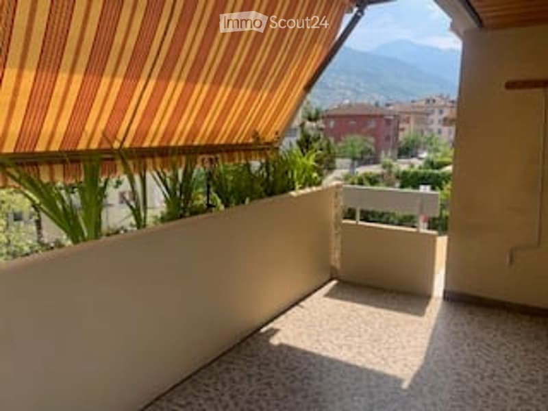 Balcony with striped awning, potted plants, and a view of the city and mountains.