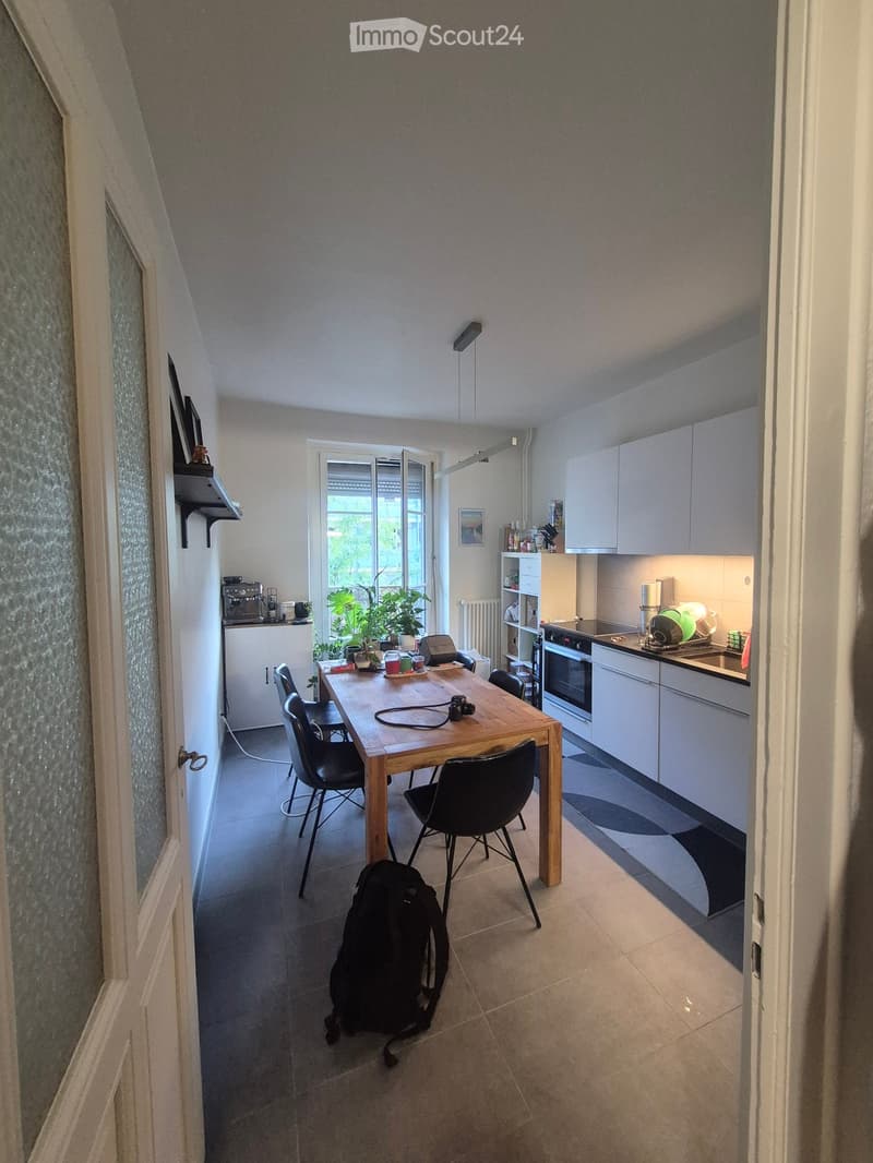 Modern kitchen and dining area with white cabinets, wooden dining table, black chairs, and various appliances.
