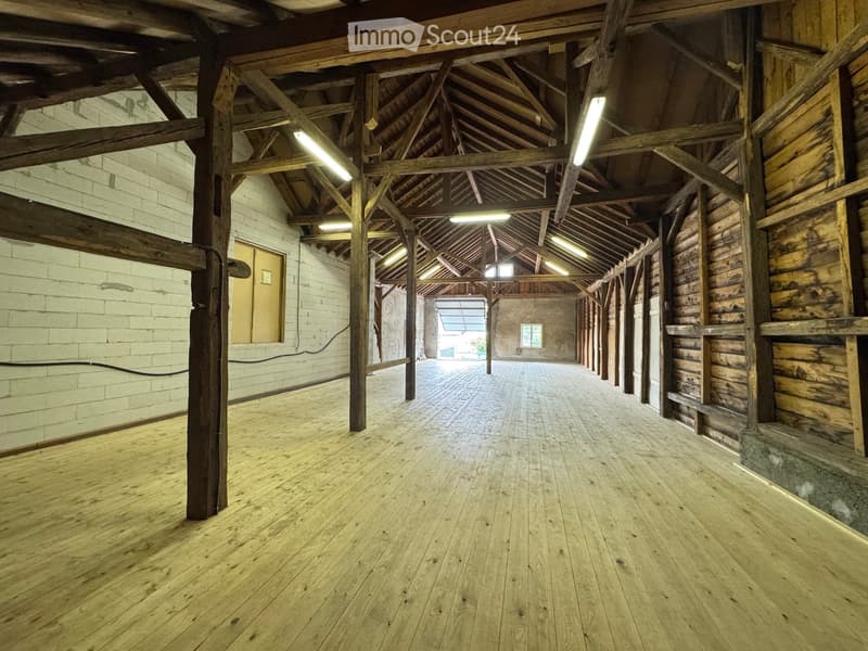 Empty wooden-floored room with exposed wooden beams and white brick walls, featuring a large open space and natural lighting from skylights.