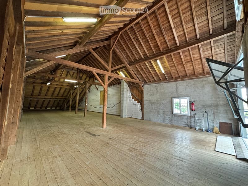 Large, open, wooden-floored space with exposed wooden beams and a high, vaulted ceiling. Minimal furnishings, with a few tools and a fire extinguisher visible.