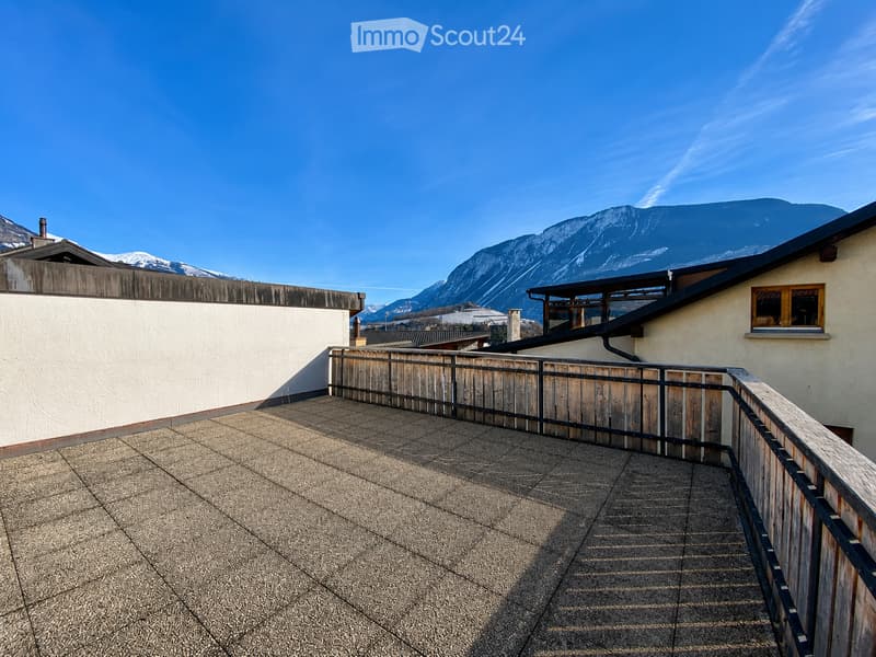 Roof terrace with tiled flooring, wooden and metal railing, overlooking a mountain range under a clear blue sky.