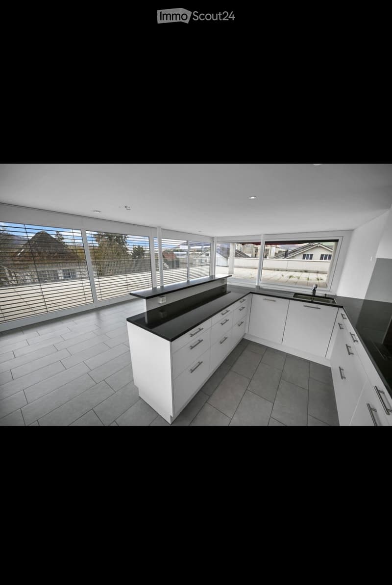 Modern kitchen with white cabinets, black countertops, and large windows offering a view of the surrounding area.