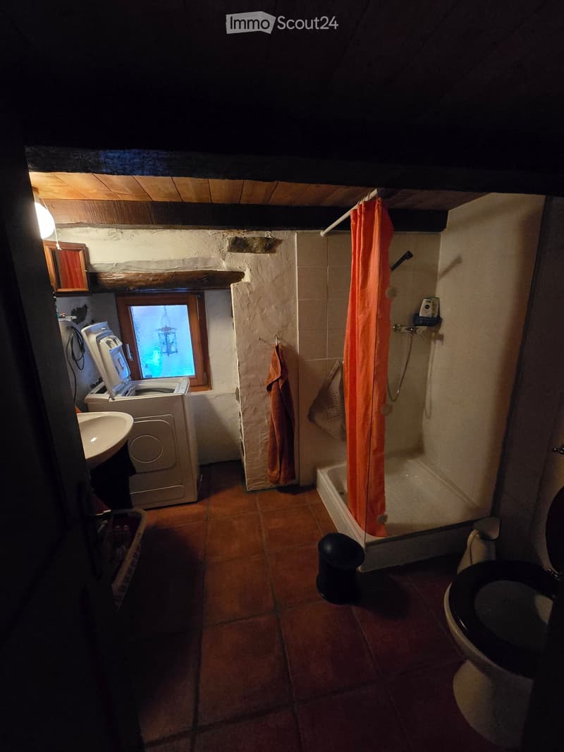 Bathroom with terracotta tiles, a toilet, bathtub with shower curtain, sink, washing machine, and a small window.