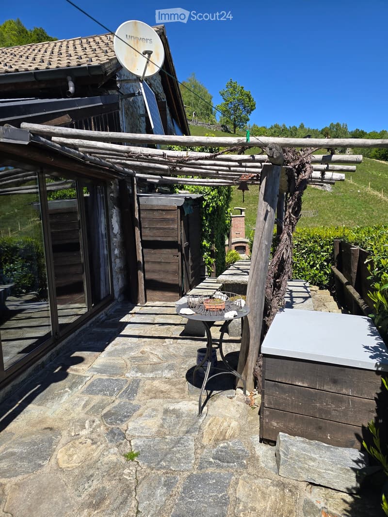 Outdoor patio area with stone flooring, wooden pergola, small table with chairs, and a basket on the table.