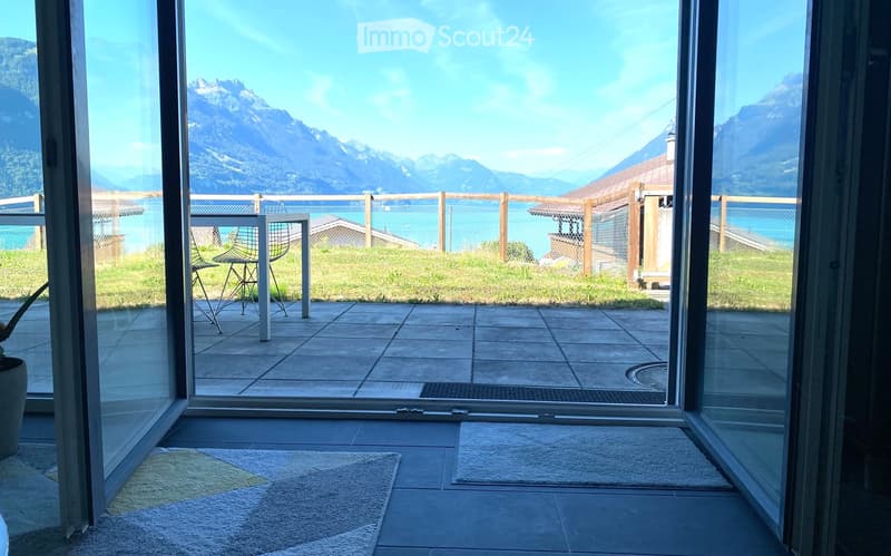 Balcony with tiled floor, overlooking a scenic mountain view and lake, with a small table and chair.