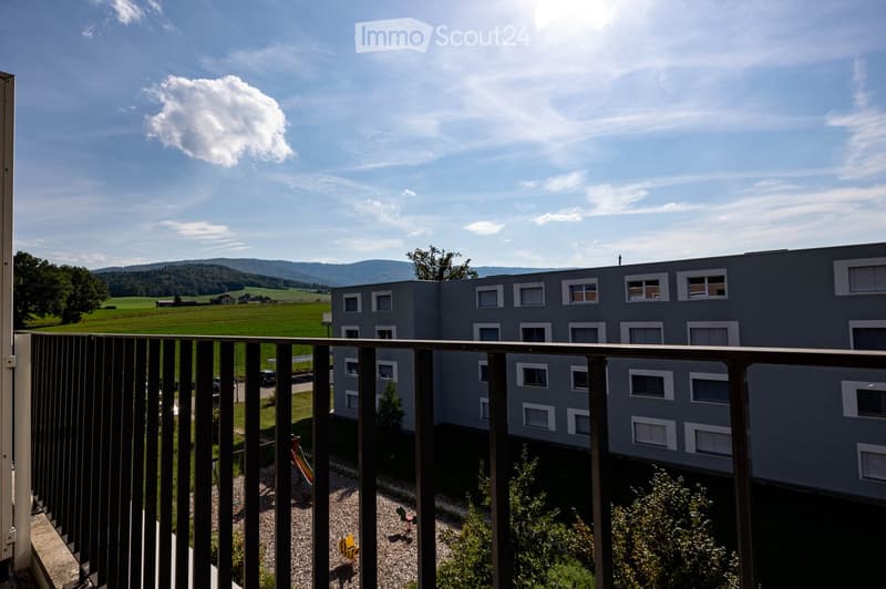 Balcony with railings, apartment building, greenery and hills in the distance