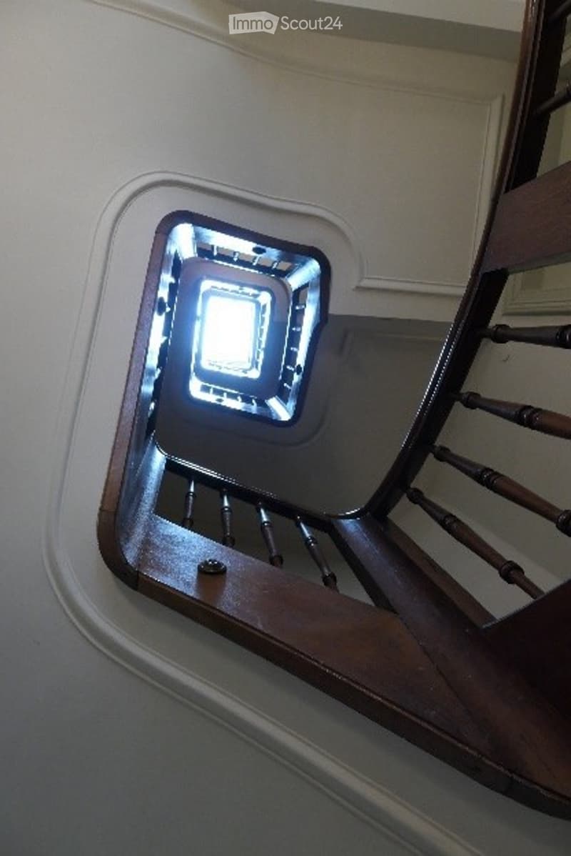 Spiral staircase with wooden handrails and a central light fixture, viewed from below.