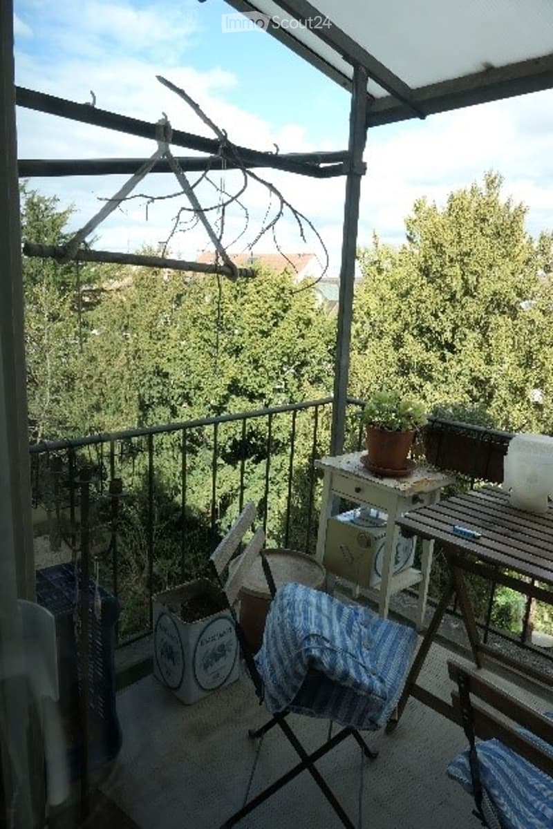Balcony with metal railing, wooden table, potted plants, and a hanging drying rack.