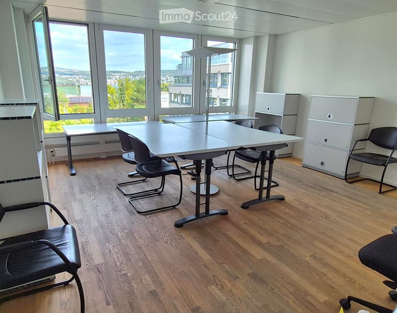 Bright, modern office space with wooden flooring, large windows offering a scenic view, and several tables and chairs arranged for meetings or collaborative work.