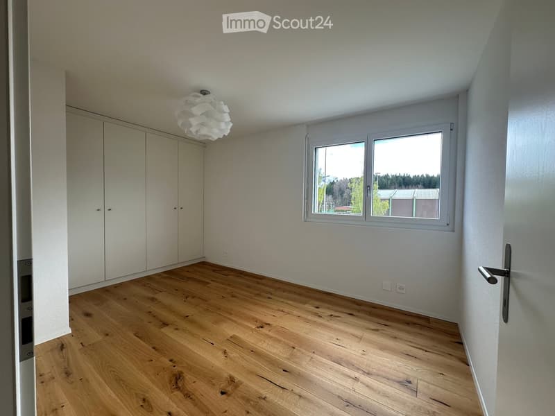 Empty room with wooden flooring, white walls, large window, and built-in closet.