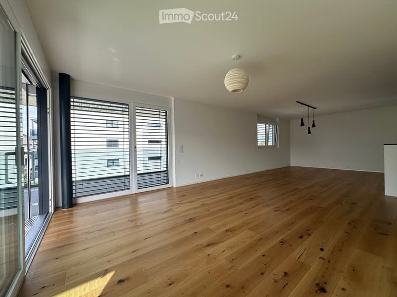 Empty room with wooden flooring, large windows with blinds, and modern lighting fixtures.