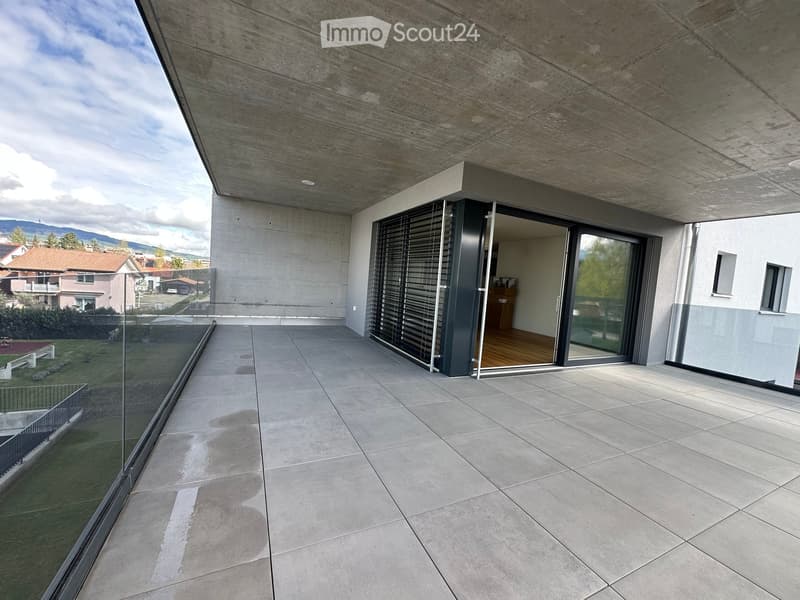 Modern balcony with large glass sliding doors, tiled floor, and a view of the surrounding area.