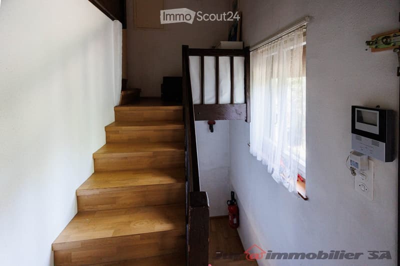 Wooden staircase with a dark wooden handrail, white walls, a window with sheer curtains, a fire extinguisher, and an intercom system mounted on the wall.