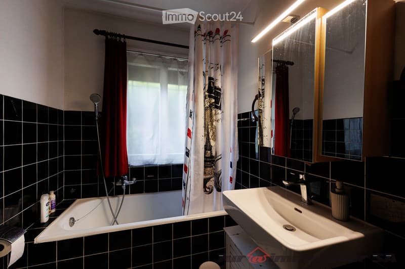 Bathroom with black tiled walls, a bathtub, a sink, a mirror, and a shower curtain with a Paris theme.