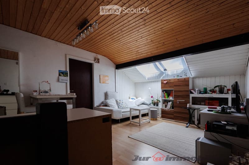 Bright, modern living room with wooden ceiling and floor, large skylight, white sofa, coffee table, bookshelf, TV, and various decorative items.
