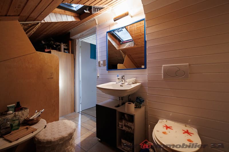 Cozy bathroom with wooden walls, a sink, a mirror, a toilet, a small stool, and a basket on the counter.